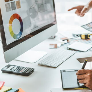 Foto eines Computer Bildschirmes auf welchem ein Kreisdiagramm angezeigt wird. Man sieht an der Seite Zwei Hände, eine der Hände zeigt auf den Bildschirm die andere schreibt etwas auf einem Tablet.